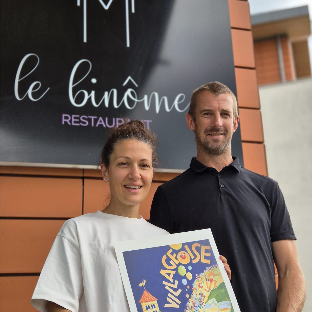 Les propriétaires du restaurant Le Binôme avec l'affiche 2025